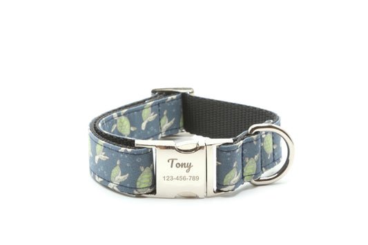 A personalized dog collar with a navy blue and green leaf pattern, a black webbed inner band, and a silver-tone metal clasp engraved with the name 'Tony' and a phone number.